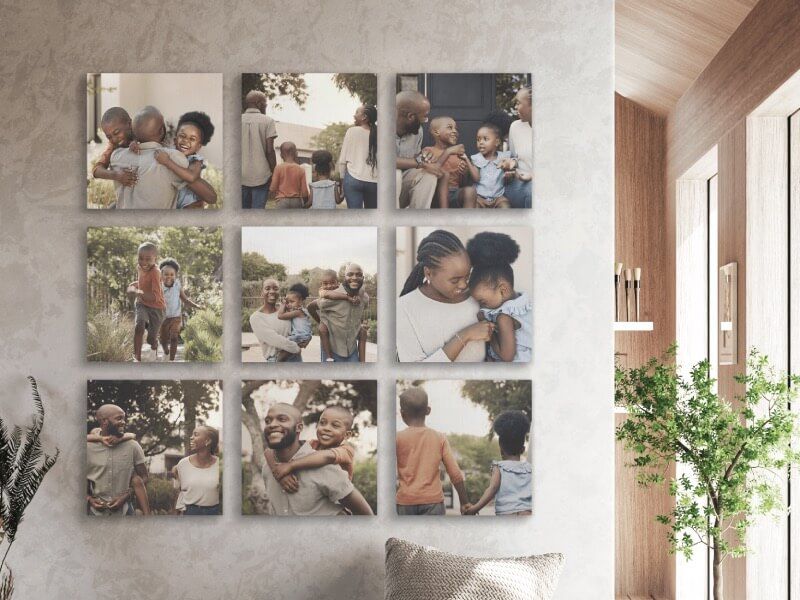 A nine-panel grid of square canvas photo prints on a wall, showing candid moments of a family with children, above a woven throw pillow and potted plants.