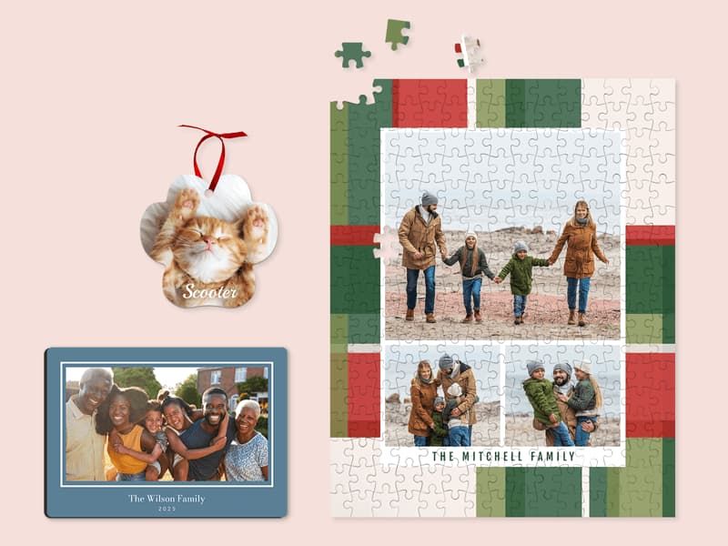 A paw-shaped cat photo ornament labeled 'Scooter' with a red ribbon, a blue photo plaque of a multigenerational family reading 'The Wilson Family,' and a plaid-bordered jigsaw puzzle of a family on the beach labeled 'The Mitchell Family.'