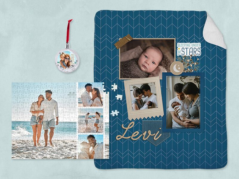 A blue chevron-pattern photo blanket personalized 'Levi' with baby photos, next to an assembled beach-photo jigsaw puzzle and a round photo ornament.